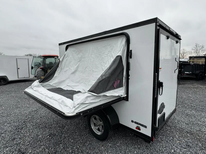 2024 Cargo Mate 5.5x10' Enclosed Toy Hauler Trailer 2990# GVW * TOY HAULER * FOLD OUT BED * WHITE BLACKOUT * SLANT V-NOSE * ALUMINUM WHEELS * .030 SCREWLESS EXTERIOR * REAR SPOILER * PLYWOOD FLOORS/WALLS * TABLE * MAX AIR COVER * EXTRA HEIGHT